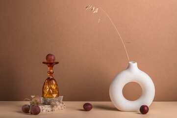 Grape berries, a wine glass and a vase with a dried spikelet on a brown background with copy space.
