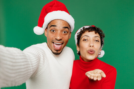 Merry young couple man woman in red casual clothes Santa hat posing do selfie shot pov mobile cell phone blow air kiss isolated on plain green background Happy New Year 2024 Christmas holiday concept