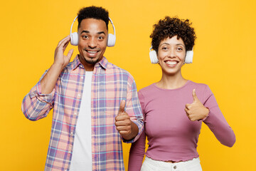 Young happy couple two friend family man woman of African American ethnicity wear purple casual clothes together listen to music in headphones show thumb up isolated on plain yellow orange background - obrazy, fototapety, plakaty