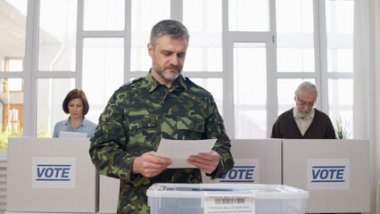 A male soldier voting at the polling place, making a choice on the ballot, and going to throw it...