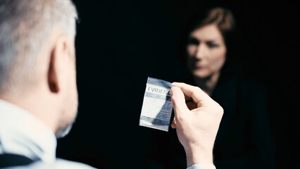 A detective is showing an evidence bag with an illegal substance to an interrogated woman - obrazy, fototapety, plakaty