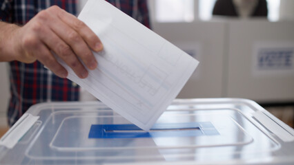 A close-up of a man about to throw a voting ballot into the sealed box during the US elections - obrazy, fototapety, plakaty