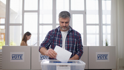A middle-aged man is voting at the polling station, throwing a ballot into the box on elections day