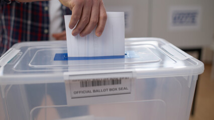 A man is throwing a voting ballot into the official ballot box, close-up, a citizen's...