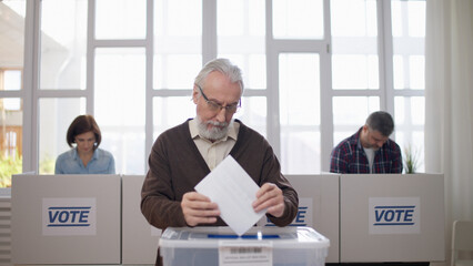 A responsible senior man is throwing a ballot into the sealed box, making his choice during the...