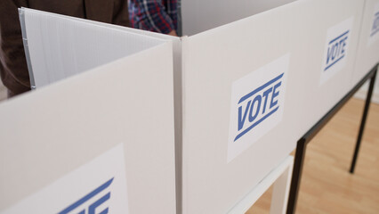 A close-up view of a voting booth, with people casting votes on ballots during election day