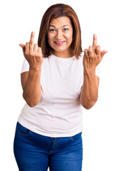 Middle age latin woman wearing casual white tshirt showing middle finger doing fuck you bad expression, provocation and rude attitude. screaming excited