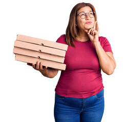 Middle age latin woman holding delivery pizza box serious face thinking about question with hand on...