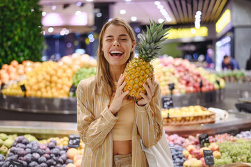 Young smiling fun customer woman wear casual clothes holding pine-apple shopping at supermaket...