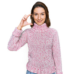 Young caucasian girl wearing wool winter sweater smiling and confident gesturing with hand doing small size sign with fingers looking and the camera. measure concept.