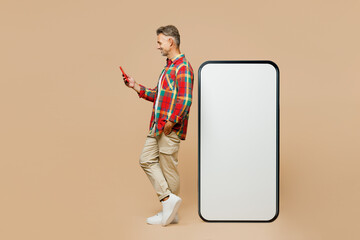 Full body profile adult man wear red shirt white t-shirt casual clothes big huge blank screen mobile cell phone smartphone with area use device isolated on plain pastel light beige color background