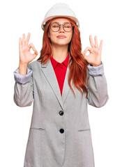 Young redhead woman wearing architect hardhat relax and smiling with eyes closed doing meditation gesture with fingers. yoga concept.