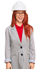 Young redhead woman wearing architect hardhat winking looking at the camera with sexy expression,...