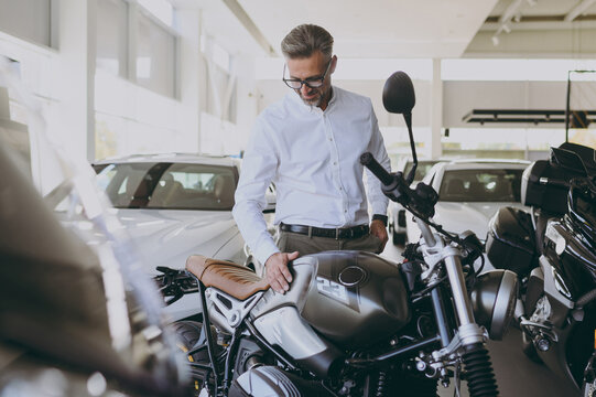 Rich adult man customer male buyer client wearing shirt choose touch gently bike want to buy new black motorbike or automobile in car showroom vehicle salon dealership store motor show Sales concept.