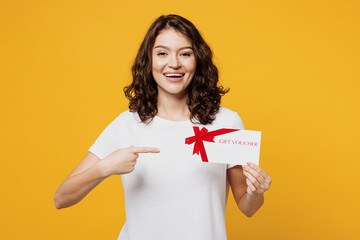 Fototapeta na wymiar Young smiling happy woman she wear white blank t-shirt casual clothes hold point finger on gift certificate coupon voucher card for store isolated on plain yellow orange background. Lifestyle concept.