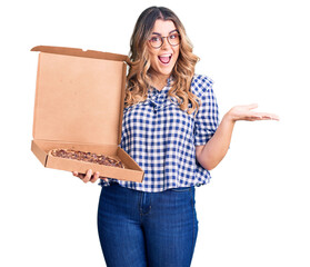 Young caucasian woman holding delivery pizza box celebrating victory with happy smile and winner expression with raised hands