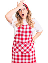 Young caucasian woman wearing apron surprised with hand on head for mistake, remember error. forgot, bad memory concept.