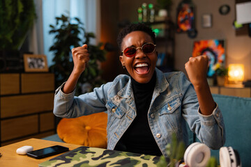 Delighted afro american woman wearing stylish pink sunglasses raising fists celebrating passing last exam at the university school. Education concept. - obrazy, fototapety, plakaty