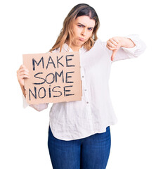 Young caucasian woman holding make some noise banner with angry face, negative sign showing dislike...