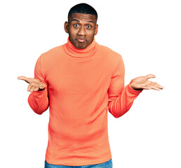 Young black man wearing orange turtleneck sweater clueless and confused expression with arms and hands raised. doubt concept.