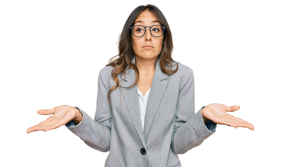 Young brunette woman wearing business clothes clueless and confused expression with arms and hands raised. doubt concept.