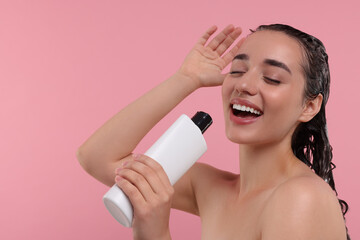Washing hair. Portrait of beautiful happy woman with bottle singing on pink background. Space for text