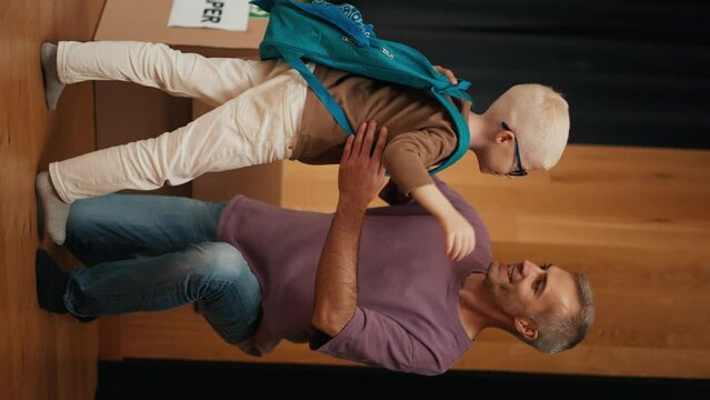 A blond boy in glasses with a green and blue backpack came with his dad to a club preparing children for school. A man with gray hair in a purple T-shirt brought his son to a club for preparing