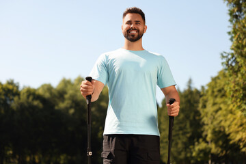 Happy man practicing Nordic walking with poles outdoors on sunny day