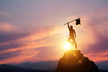 Silhouette of a businessman jumping with a flag on the mountain and sunset light. concept of...