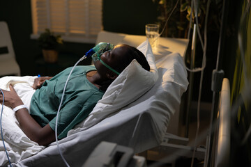 Close-up of the African woman's face in the hospital bed, wearing an oxygen mask, looking calm and...