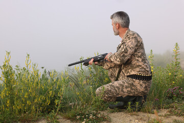 Man wearing camouflage with hunting rifle outdoors. Space for text
