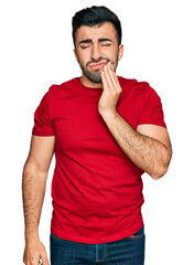 Hispanic man with beard wearing casual red t shirt touching mouth with hand with painful expression because of toothache or dental illness on teeth. dentist