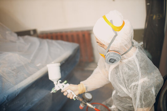 Car painter in protective clothes and respirator mask painting vehicle
