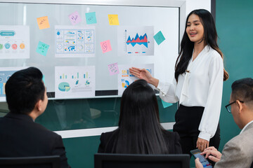 A female leader presenting growth Statistics with confident in front of whiteboard rounded by executive committee listening data analyst and business plan. Conference room meeting. Intellectual. - obrazy, fototapety, plakaty
