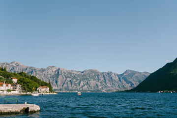 Boats sail past the coast of Perast against the backdrop of a high mountain range. Montenegro