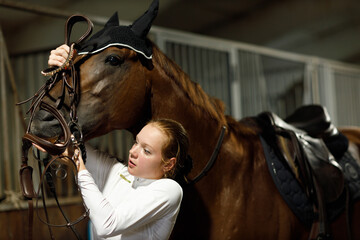 Woman rider jockey at stable preparing puts on the bridle horse racing or jumping competition