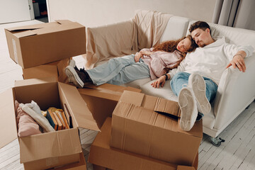 Young family couple man and woman relaxing on sofa after moving cardboard boxes to new estate home...