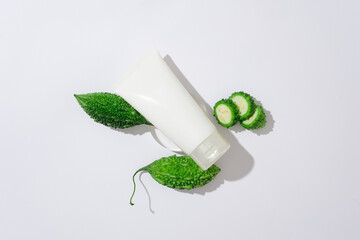 Minimal mockup scene for advertising cosmetic with bitter melon extract. Top view of a white plastic tube with fresh bitter melon and bitter melon slices displayed on a white background