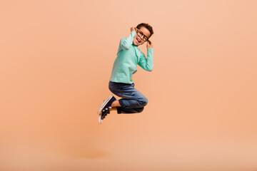 Full length portrait of energetic carefree schoolkid jumping arms touch eyeglasses isolated on beige color background
