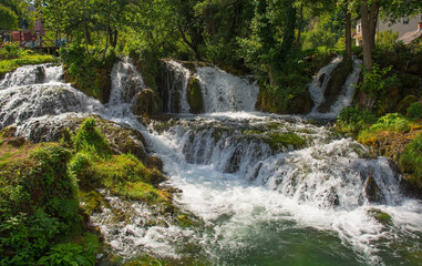 Fototapeta na wymiar A small waterfall in a stream which runs through the village of Martin Brod in Una-Sana Canton, Federation of Bosnia and Herzegovina. Located within the Una National Park. Early September