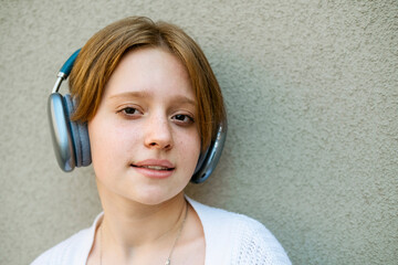 Portrait of a teenage girl in headphones against a gray wall. 