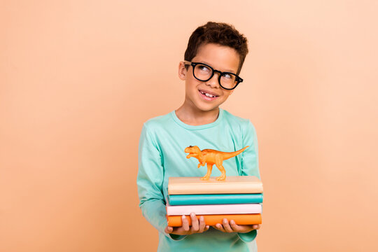 Photo of preeten age cute latin boy wear trendy clothes hands hold book dino toy empty space isolated on beige color background