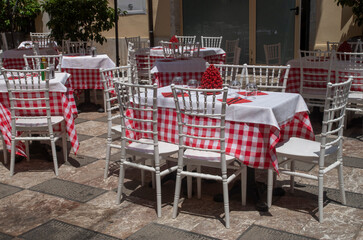 Tables with red and white checkered tablecloths and red ceramic cone in an outdoor restaurant in Sicily