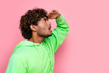Side photo of young funny guy wearing green sweatshirt touch forehead look far away copyspace information isolated on pink color background