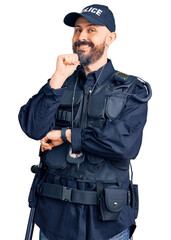 Young handsome man wearing police uniform looking confident at the camera smiling with crossed arms and hand raised on chin. thinking positive.