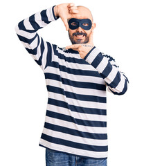 Young handsome man wearing burglar mask smiling making frame with hands and fingers with happy face. creativity and photography concept.