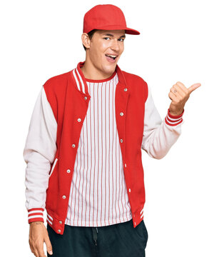 Handsome caucasian man wearing baseball uniform smiling with happy face looking and pointing to the side with thumb up.