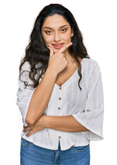 Brunette young woman wearing casual clothes looking confident at the camera smiling with crossed arms and hand raised on chin. thinking positive.