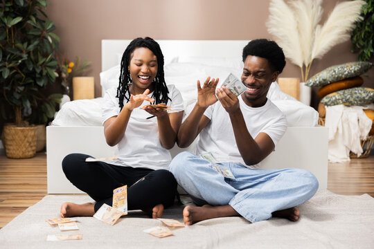 Portrait Of Cheerful Young African American Black Dark Skinned Couple Holding Money Celebrating Success Together Throwing In Air.