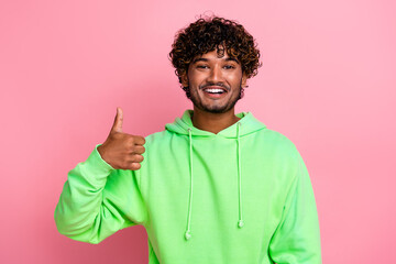 Portrait of positive promoter young student indian guy wearing green sweatshirt makes like sign thumb up isolated on pink color background